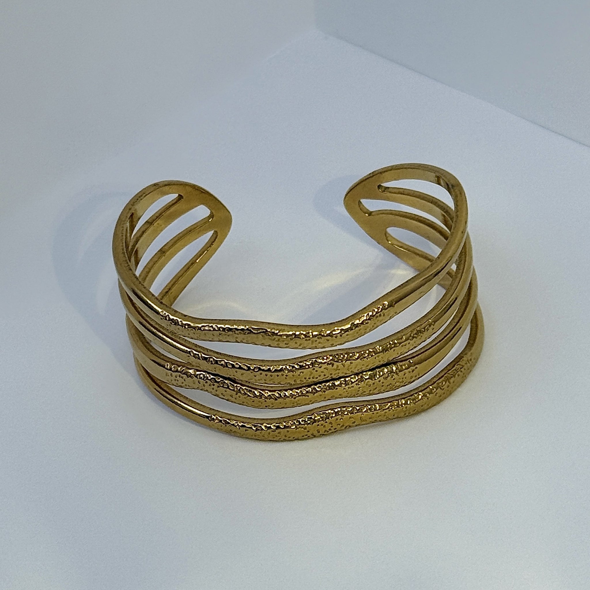 Pulseira aberta em aço dourado com textura ondulada
